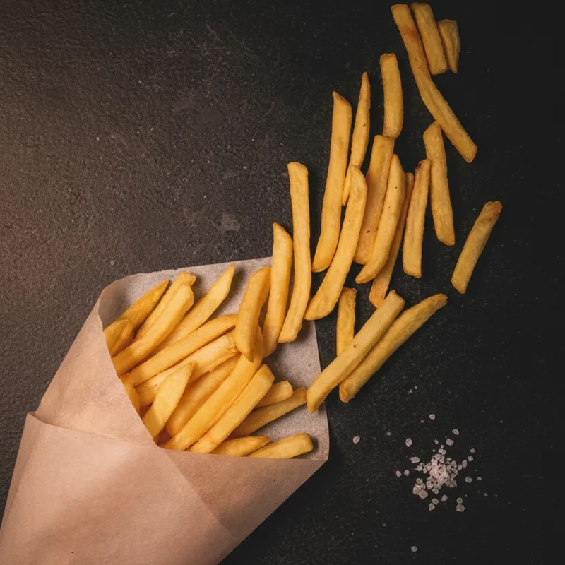 Golden french fries spilling from a paper cone on dark stone